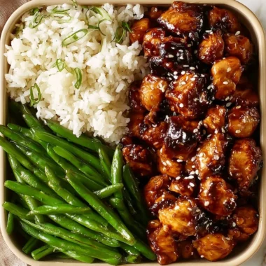 High protein sesame chicken dish garnished with sesame seeds and green onions.