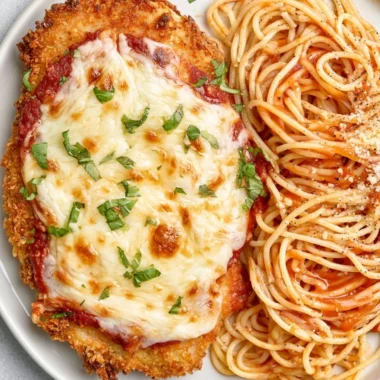 Baked Chicken Parmesan topped with melted cheese and fresh basil on a plate.