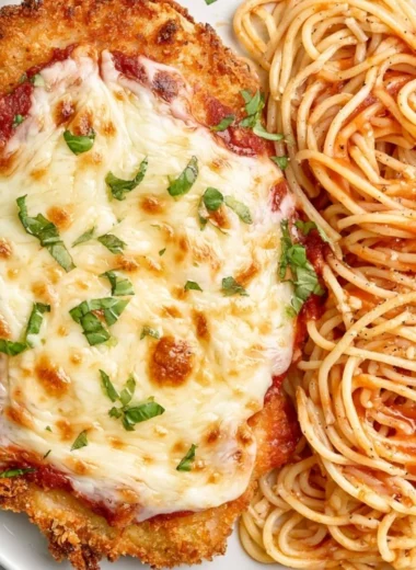 Baked Chicken Parmesan topped with melted cheese and fresh basil on a plate.