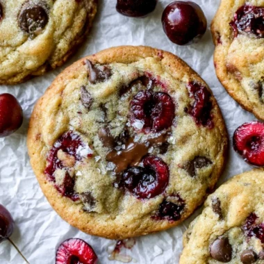 Batch of cherry chocolate chip cookies on a plate, garnished with cherries.