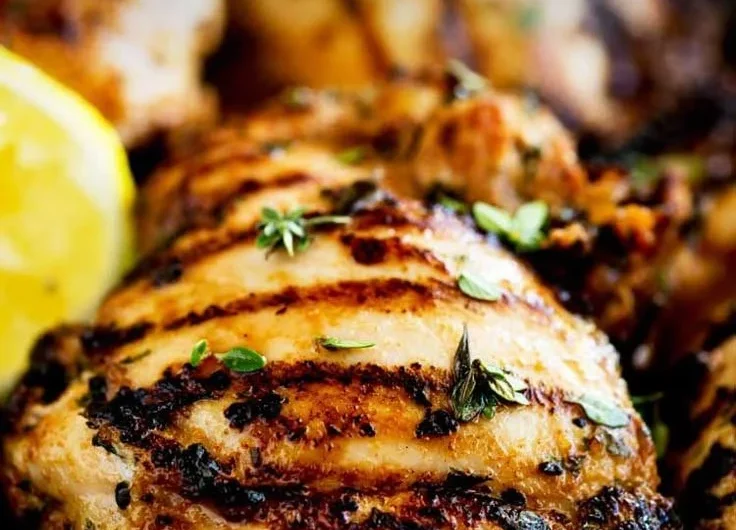Grilled apple cider thyme chicken garnished with herbs and served on a plate
