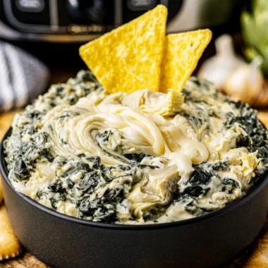 Cozy crock pot spinach artichoke dip served in a bowl with tortilla chips.