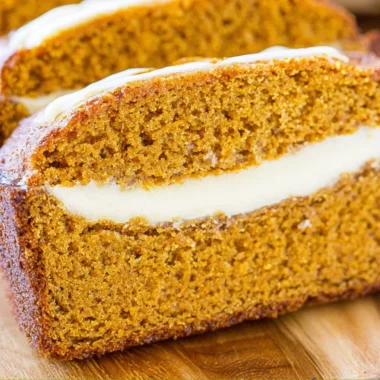 Loaf of cozy pumpkin bread topped with creamy cheese frosting on a rustic table