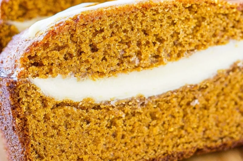 Loaf of cozy pumpkin bread topped with creamy cheese frosting on a rustic table